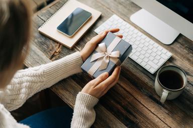 Unrecognizable woman holding a gift box while sitting at a working office desk.